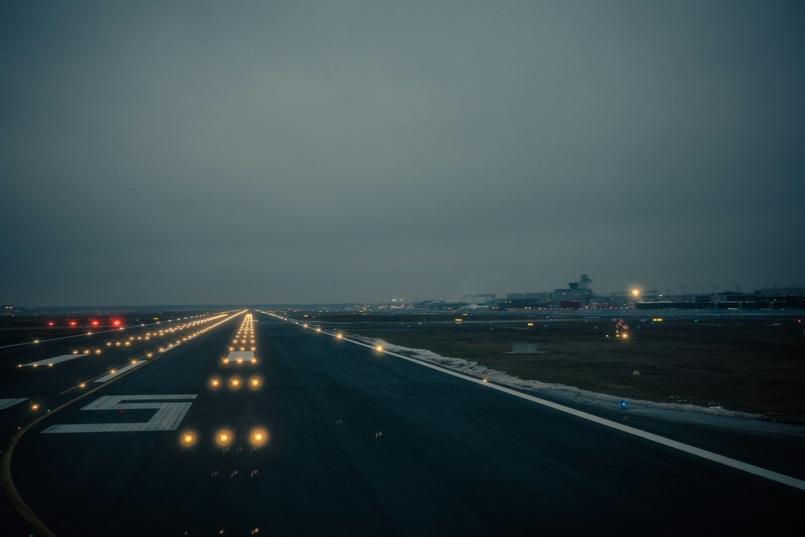 Piste d’aéroport balisée de feux, au crépuscule.