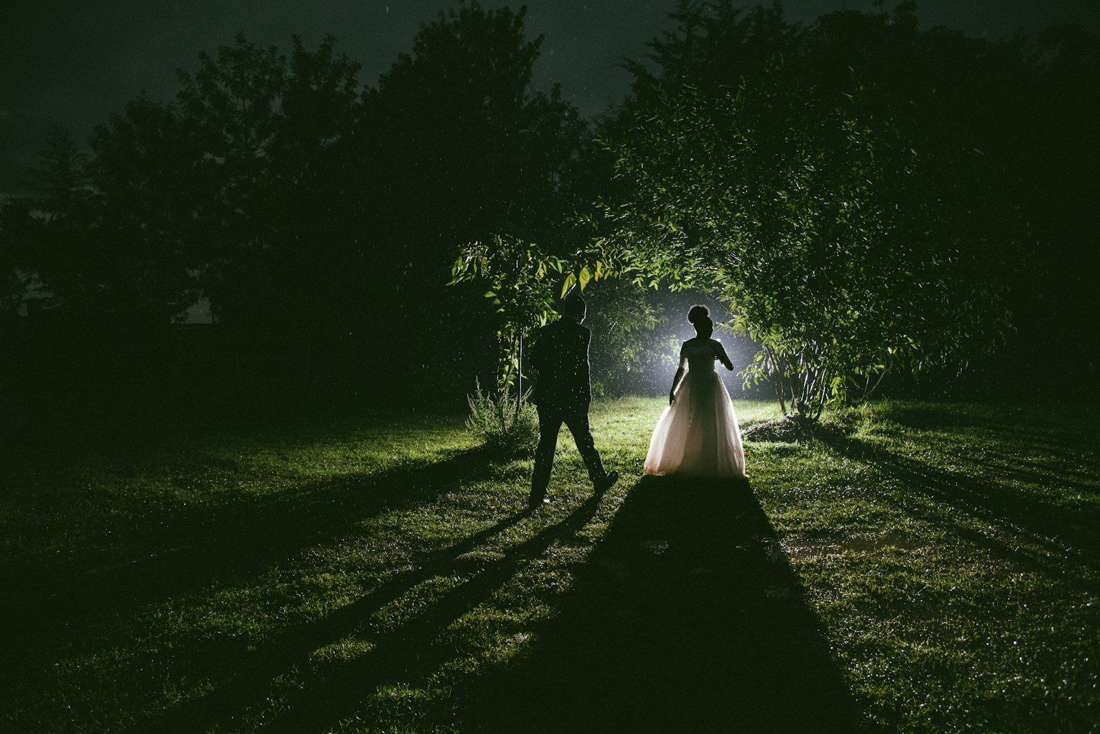 Couple de mariés en contre-jour dans un jardin, de nuit.
